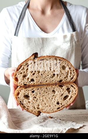 Crop faceless Woman hands holding freshly baked sourdough rye bread Crumb white cutting in half Stock Photo