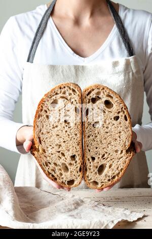 Crop faceless Woman hands holding freshly baked sourdough rye bread Crumb white cutting in half Stock Photo