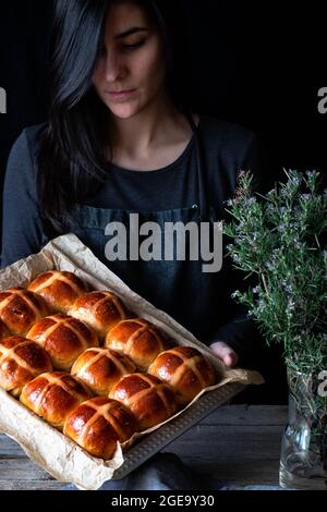 Female baker holding puff freshly baked hot cross buns on baking tray Stock Photo