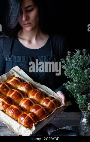 Female baker holding puff freshly baked hot cross buns on baking tray Stock Photo