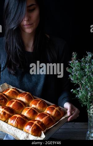 Female baker holding puff freshly baked hot cross buns on baking tray Stock Photo