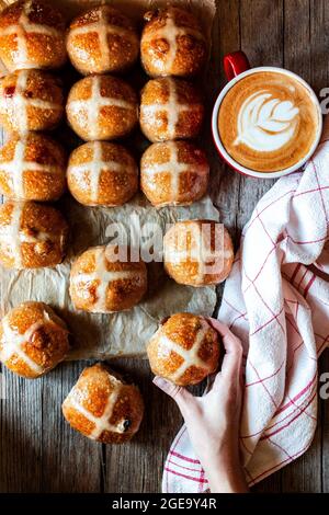 From above hand with appetizing freshly baked sourdough hot cross buns and mug of coffee on wooden table Stock Photo