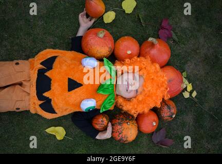 cute boy 4 years old in orange pumpkin suit lies on grass. There are many small pumpkins around it. Seasonal autumn harvest. Agriculture. Delicious he Stock Photo