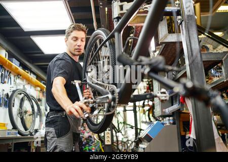 From below focused male mechanic using socket wrench and repairing bicycle wheel in workshop Stock Photo