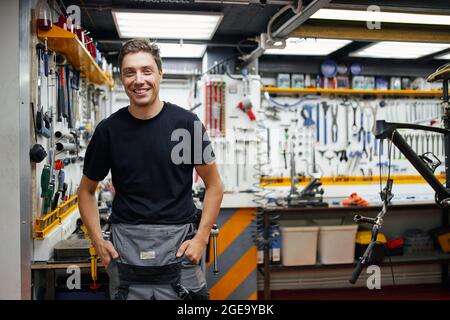 Happy male mechanic smiling and looking at camera against wall with tools in garage Stock Photo