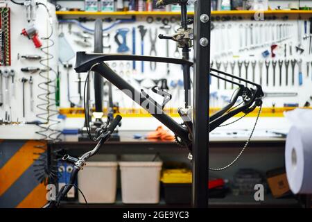 Frame of modern bike hanging on rack against workbench and wall with tools in repair workshop Stock Photo