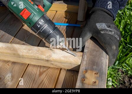 Close up of man using cordless screwdriver to fix screw into wood. Stock Photo