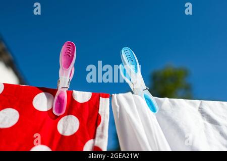 Two brightly coloured pegs holding washing on a line in bright sunshine. Stock Photo