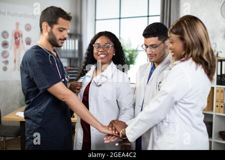 Unity and teamwork concept where four doctors and nurses in a medical team stacking hands together. Team of professional multiracial diverse medical workers in hospital ready to start their day Stock Photo