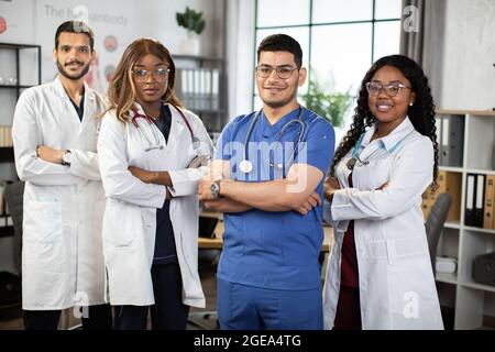 Portrait of confident multiethnical medical team, standing with arms crossed at hospital. African American, Indian and Arabian medical students posing at camera in modern conference room Stock Photo