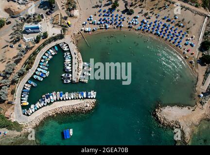 Aerial drone view of beach with people swimming and fishing boats moored at the harbor. Protaras Paralimni Cyprus Stock Photo