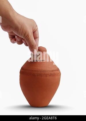 Putting a coin into a clay money box (Gullak) on white isolated background: investments, retirement fund and banking concept. Stock Photo