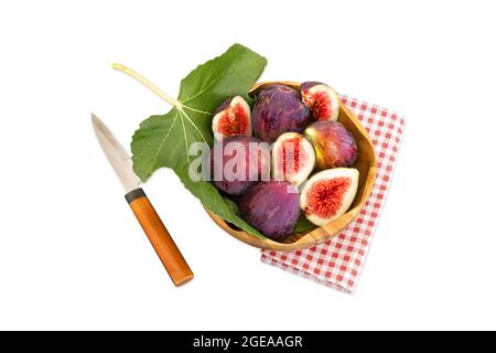 Fresh organic figs and fig leaf  in a wooden bowl with red checkered napkin and cutting knife, isolated on a white background. Fresh figs. Whole figs Stock Photo