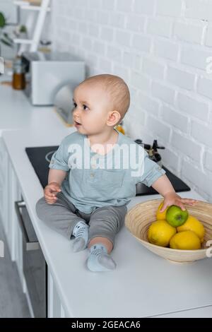 Toddler girl holding apple on kitchen worktop Stock Photo
