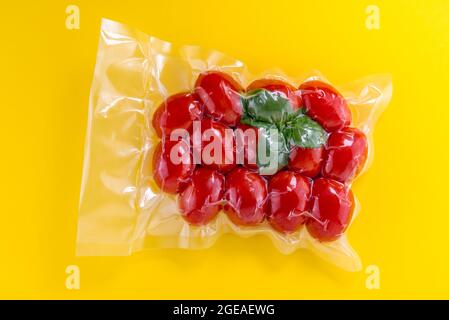Cherry tomatoes with basil leaves in vacuum packed sealed for sous vide cooking, isolated on yellow background Stock Photo