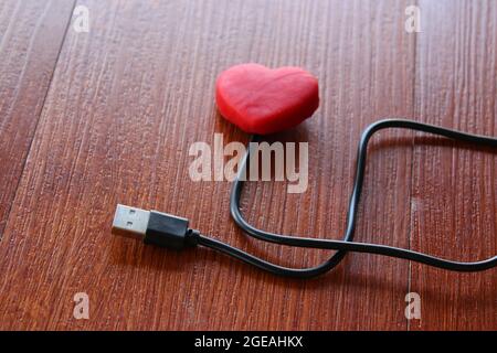 Red heart with usb cable on wooden background. Love and technology concept Stock Photo