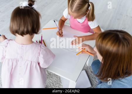 high angle view of kids drawing on papers near kindergarten teacher Stock Photo