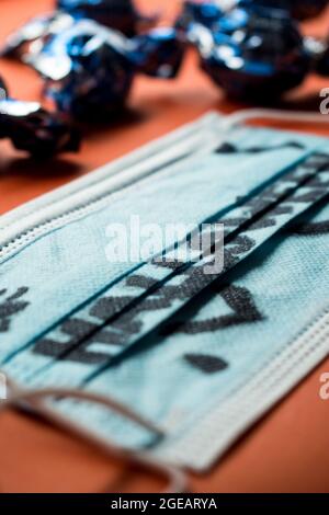 Halloween word written on a medical mask  and some chocolates in their wrappers on a orange surface Stock Photo