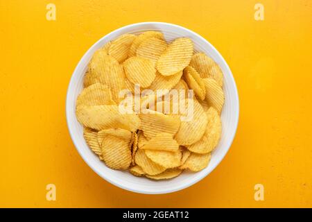 Riffled potato chips or crisps in bowl isolated on yellow background, top view Stock Photo