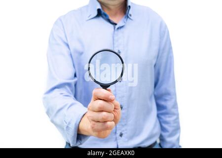 Man in blue shirt with magnifying glass in hand in front of body. Photo on white background. Copy space. Stock Photo