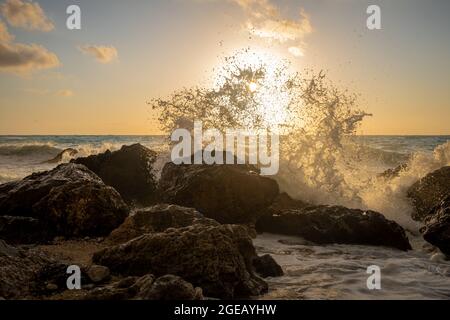 Waves crushing onto beach rocks with sun setting under the horizon. Stock Photo