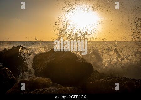 Waves crushing onto beach rocks with sun setting under the horizon. Stock Photo