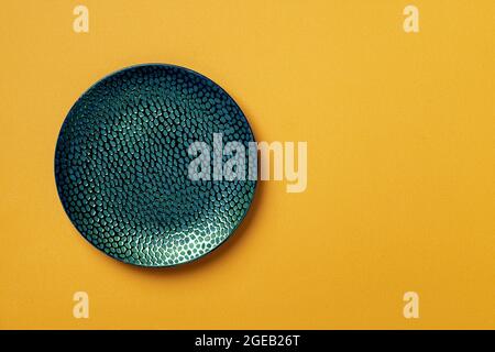 Textured turquoise teal round plate on a textured yellow background. Modern ceramic crockery and tableware for stylish food design. Empty dishes. Stock Photo