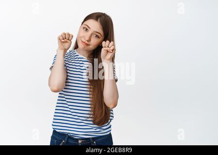 Cute young woman showing kawaii paws gesture and making coy face expression, standing against white background Stock Photo