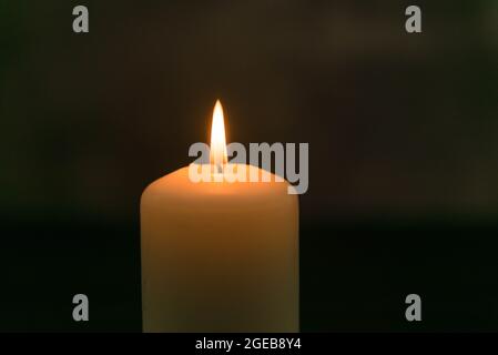 White candle in the dark on a dark background. The candle flame radiates warm yellow light. Stock Photo