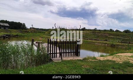 Wooden ship skeleton at the green hill near calm lake. Stock Photo