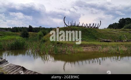 Wooden ship skeleton at the green hill near calm lake. Stock Photo