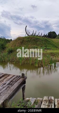 Wooden ship skeleton at the green hill near calm lake. Stock Photo