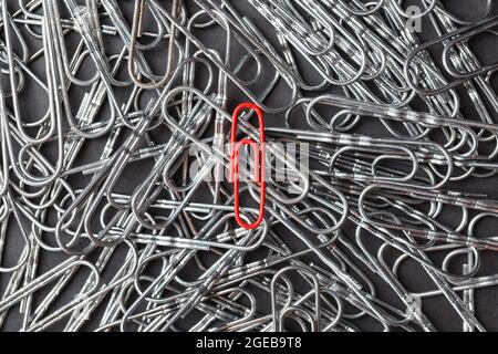 A red paper clip stands out against a textured background of silver paper clips. Concept Stock Photo