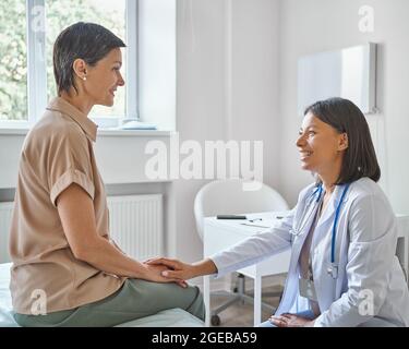 Young smiling caring african female doctor supporting comforting happy middle-aged woman patient Stock Photo