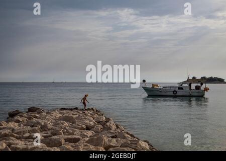 Rogoznica, Croatia-July 11th, 2021: Small boy jumping and playing on he stone pier in the bay of Rogoznica, in the evening hours, before incoming stor Stock Photo