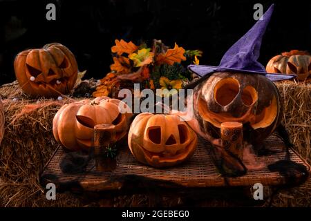 Halloween Many carved pumpkins lantern Jack for the holiday stands on a straw. Composition of scary pumpkins and candles on a dark background for the Stock Photo