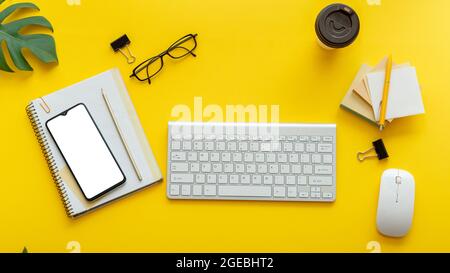 Office table desk with computer keyboard glasses, smartphone mouse office supplies plants coffee cup. Flat office workspace on colorful yellow Stock Photo
