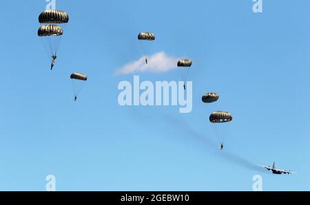 Soldiers with the 294th Quartermaster Company, 338th Quartermaster Company, Texas Army National Guard, the 3rd Special Forces Group, soldiers with the Latvian Army’s Special Forces Group and British Army’s 4th Battalion, Parachute Regiment (4 PARA), jump and parachute out of a C-130 Hercules aircraft over Camp Grayling Joint Maneuver Training Center, Grayling, Michigan, Aug. 13, 2021. The service members conducted joint airborne training during Northern Strike 21, which is an opportunity to build readiness and interoperability with other units and multinational partners while training in reali Stock Photo