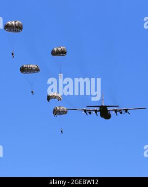 Soldiers with the 294th Quartermaster Company, 338th Quartermaster Company, Texas Army National Guard, the 3rd Special Forces Group, soldiers with the Latvian Army’s Special Forces Group and British Army’s 4th Battalion, Parachute Regiment (4 PARA), jump and parachute out of a C-130 Hercules aircraft over Camp Grayling Joint Maneuver Training Center, Grayling, Michigan, Aug. 13, 2021. The service members conducted joint airborne training during Northern Strike 21, which is an opportunity to build readiness and interoperability with other units and multinational partners while training in reali Stock Photo