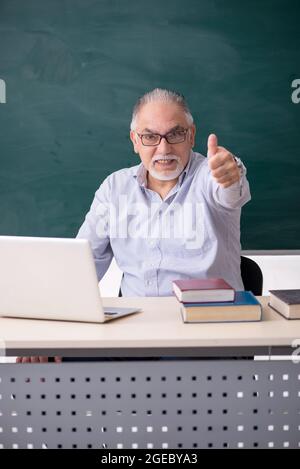Old teacher in front of green board Stock Photo