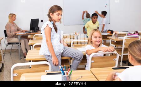 Cheerful preteen classmates talking at recess between lessons Stock Photo
