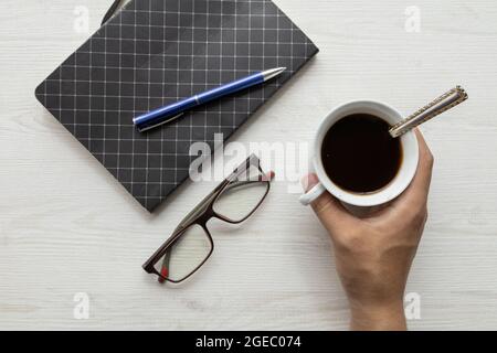 closed notebook with a blue pen next to glasses and cup of coffee with spoon, lifestyle in workspace, studio Stock Photo