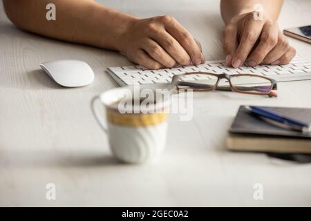 studio with a person working, detail of a person's hands typing on his modern keyboard, desk with glasses, pen, cup of coffee, computer mouse,keyboard Stock Photo