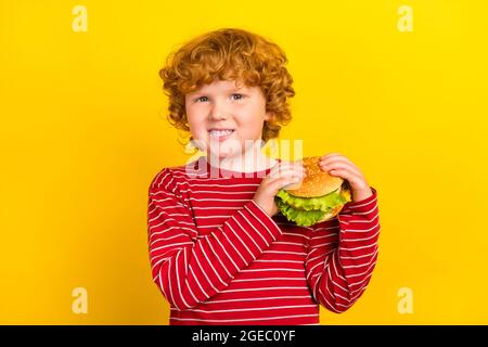 Photo of young happy positive cheerful small boy hold hands cheeseburger smile isolated on yellow color background Stock Photo