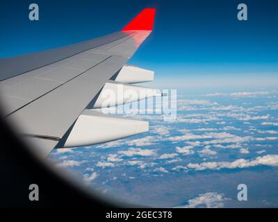 Wing of flying plane from passenger cabin window in blue sky Stock Photo