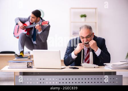 Young employee playing guitar in the presence of old boss Stock Photo