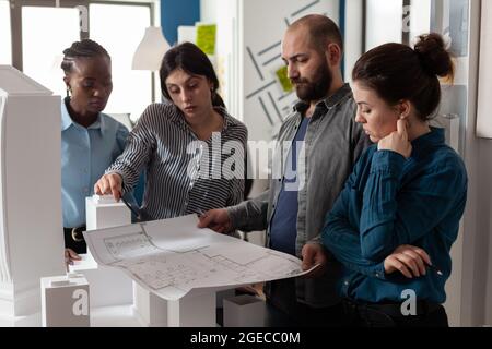 Team of multi ethnic architects designing blueprint plan for construction project design. Workers analyzing maquette buildng model engineering technology at professional office. Stock Photo