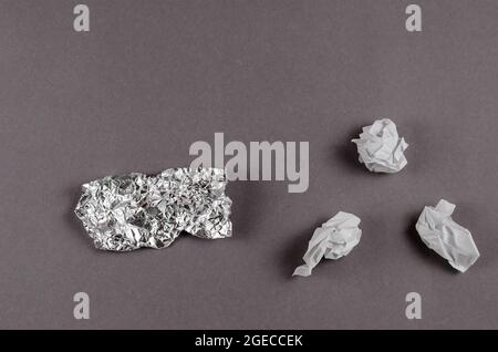 Minimalist composition with crumpled foil and white paper against a gray background. Pieces of aluminum foil and paper randomly on a monochrome backgr Stock Photo