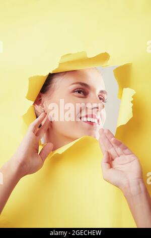 Excited young Caucasian woman standing behind ripped banner and gesturing hands for photo Stock Photo