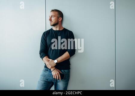 Young man leaning to a wall and looking away. Thoughtful male professional in office. Stock Photo